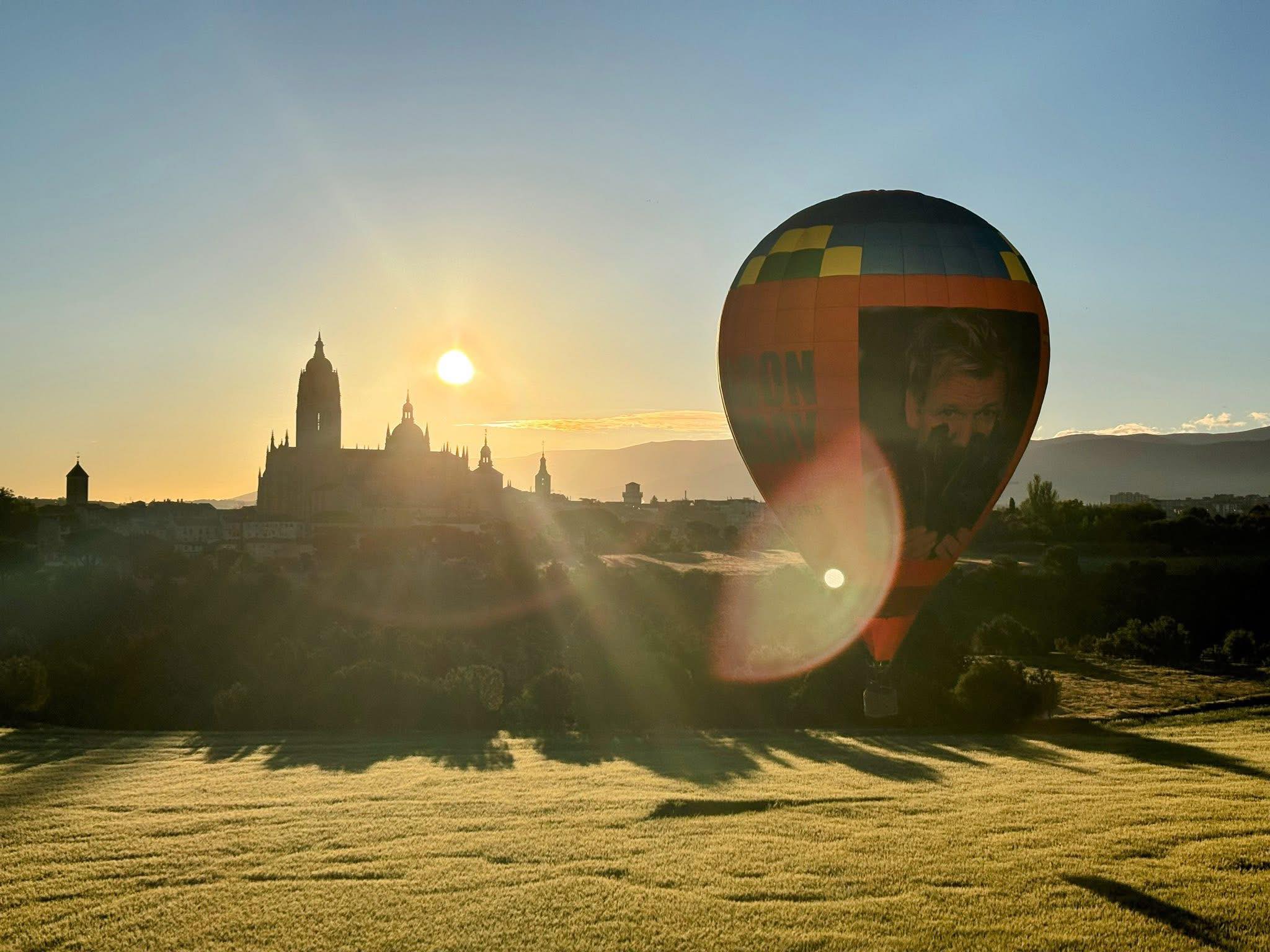 Hot air balloon over Segovia at sunrise, with the cathedral silhouetted against the sky